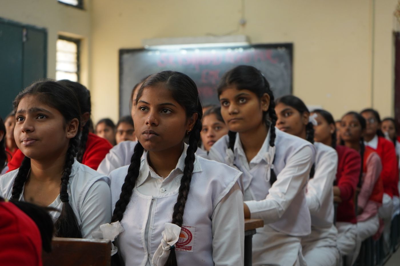 Schoolgirls in white uniforms listening attentively in their classroom.