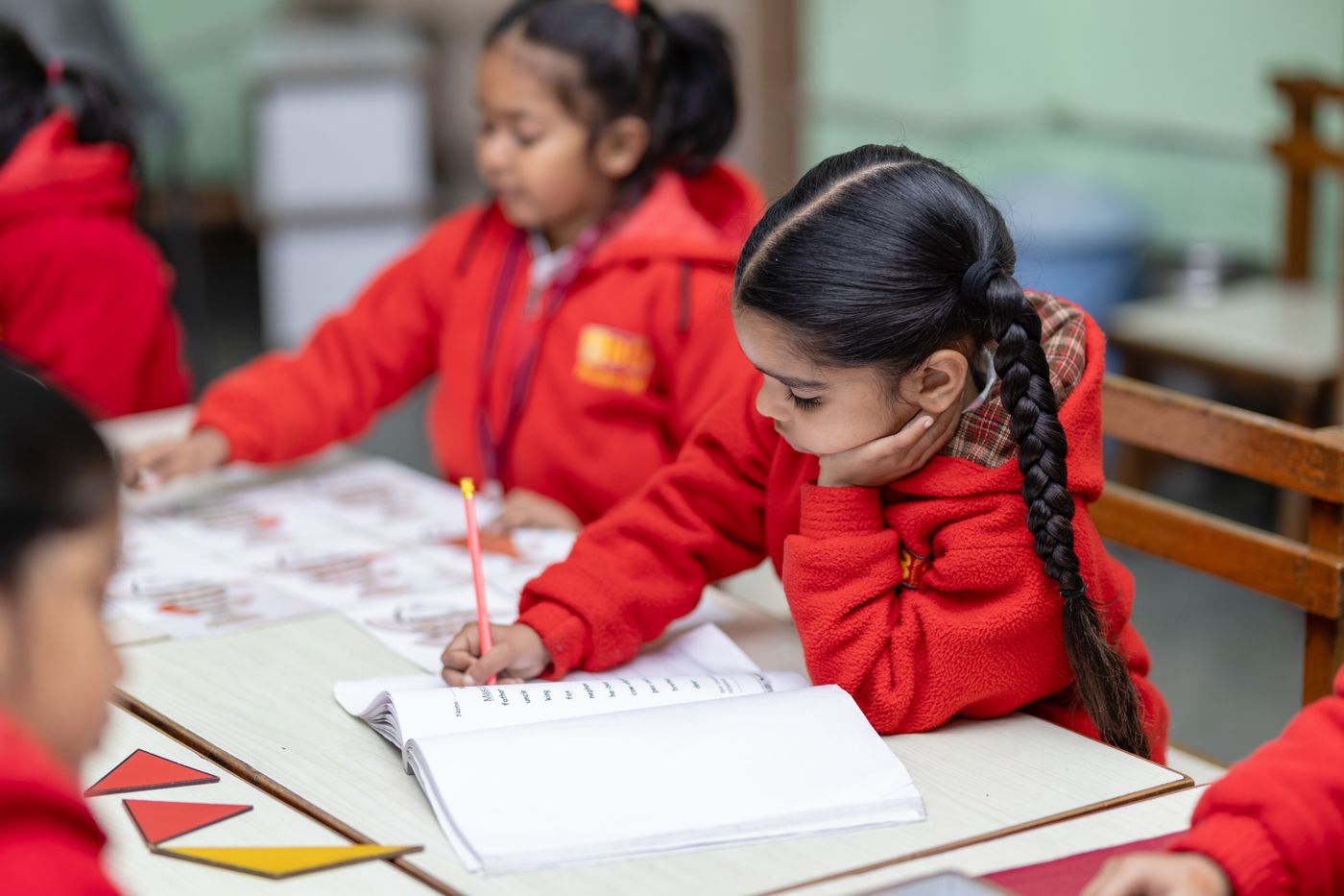 A schoolgirl in a red school uniform writing carefully at her desk.