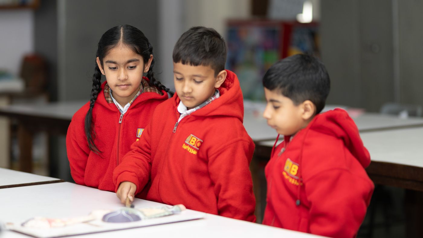 Young students in red school uniforms working together at a classroom table.